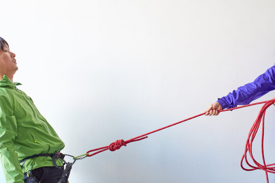 白い壁の前でカラビナがかかったハーネスを引っ張られる登山者