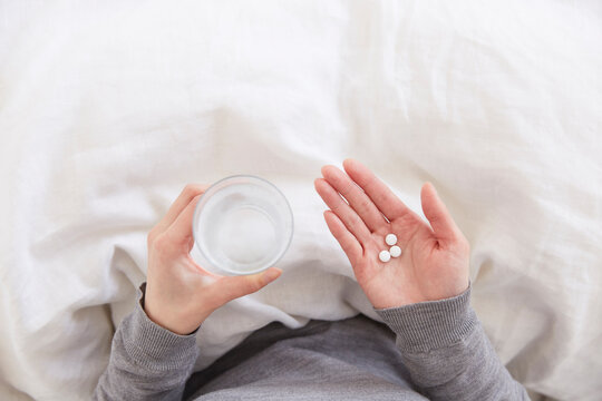 布団の上で錠剤と水を持つ女性の手