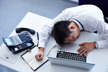 デスクに倒れこみ辛い表情をする男性