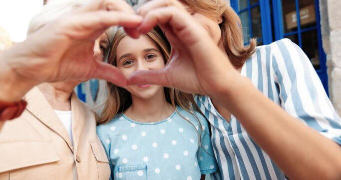 Close up of cute teenage girl looking at camera smiling through heart shape folded by her mom and grandma.