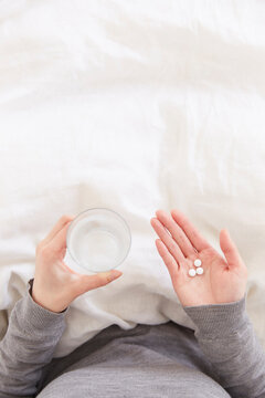 布団の上で錠剤と水を持つ女性の手