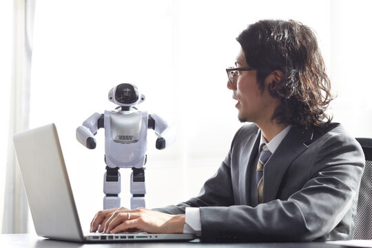 パソコンをしながらロボットと話す男性