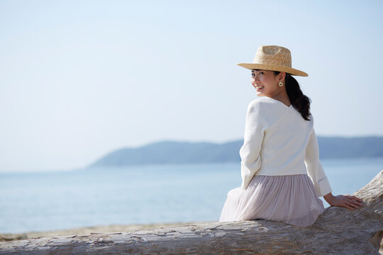 海辺の流木に座って振り向く女性 ,日本,和歌山県,和歌山市,加太周辺
