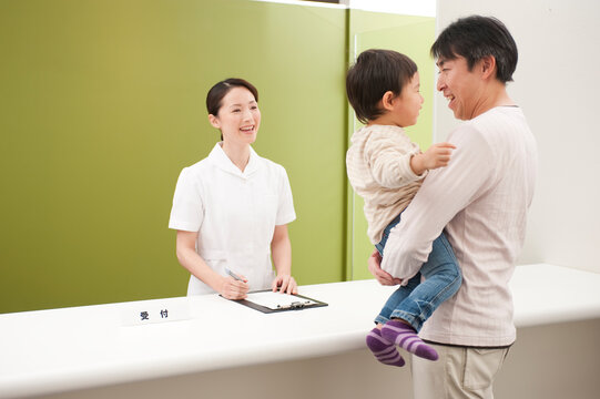 病院の受付で受診受付をする女性事務員と子供を抱いた男性