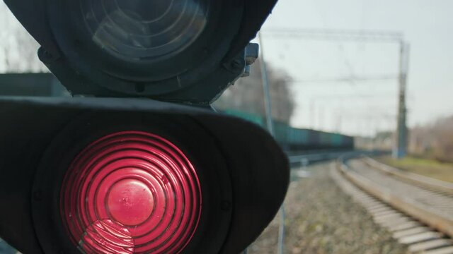 A semaphore with a red signal on a railway stretch. A long freight train passes out of focus in the background. Well-established operation of all systems on the railway.