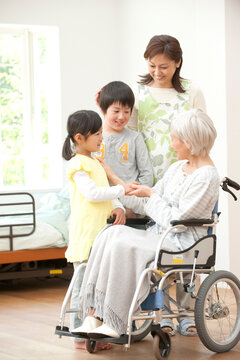 車椅子のシニア女性と介護ヘルパーと孫男女