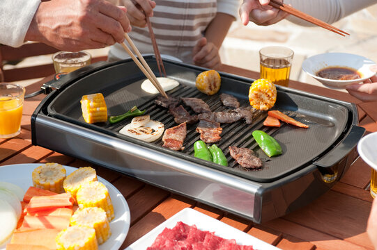 ホットプレートで焼肉をする箸を持つ家族の手