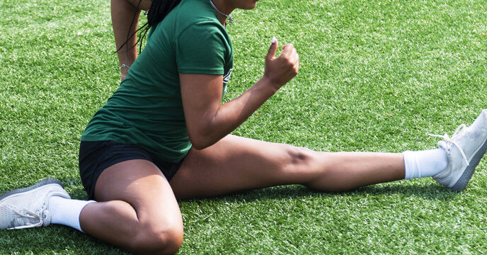 Close Up Of Female Athlete In A Hurdlers Stretch On A Green Turf Field