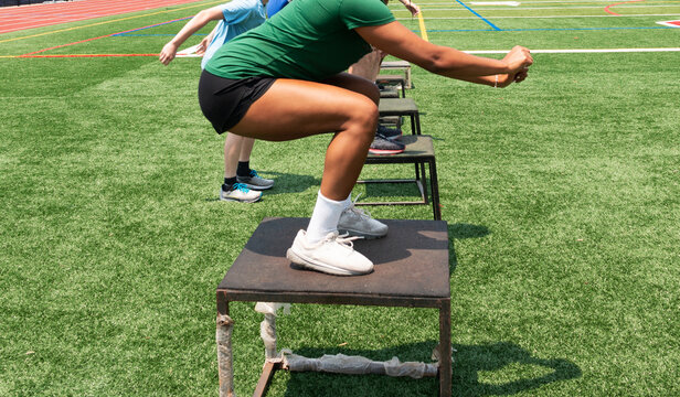 Athletes jumping on to plyo boxes outdoors on a turf field - Powered by Adobe