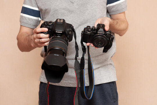 Man is holding in one hand dslr camera Canon and mirrorless Olympus in another one. Comparison of two cameras for shooting. Choosing before buying and evaluating the pros and cons of cameras