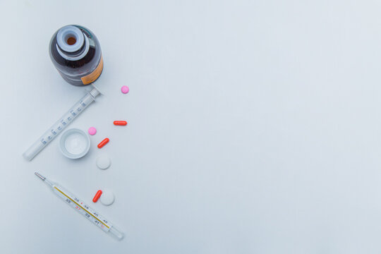 A medicine with a measuring syringe, tablets and capsules and a thermometer lies on the side against a white background. High quality photo