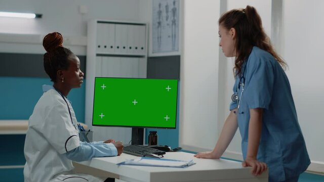 Group of doctor and nurse working with green screen on monitor in doctors office. Medical team looking at computer with chroma key and mockup isolated template or background on display.