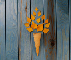 Yellow autumn leaves in a waffle cone on a blue wooden background Autumn composition.
