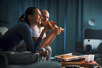 Happy couple sitting on the couch and eating pizza together