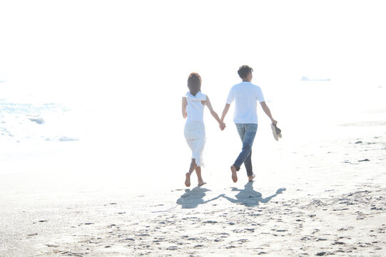 海辺を裸足で歩くカップル後姿