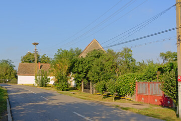 Fototapeta na wymiar Street in the old Rromanian village Aurel Vlaicu, with electricity pole with stork nest and mountains in the background on a sunny day with clear blue sky 