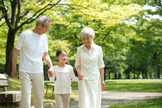 公園を散歩するシニア夫婦と孫