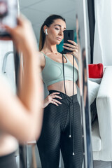 Athletic girl taking pictures in front of the mirror while resting from exercising at home