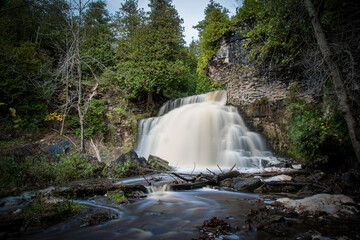 The milky water of Jones Falls near Owen Sound, Ontario cascades down the rocky cliff and through the surrounding forest. - obrazy, fototapety, plakaty