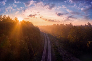 Railway road in the middle of foggy autumn forest in bright sunshine at dawn. Beautiful landscape...