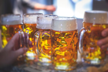 View of beer festival, gold coloured beer glasses assortment in a pub, german unfiltered wheat beer, people cheering up and toasting with glasses of light lager, Oktoberfest view