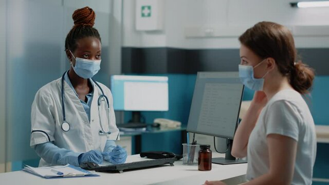 Medical specialist discussing healing treatment with ill woman in doctors office. Doctor doing medical consultation with patient while wearing face masks for protection against pandemic