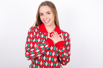 Honest Young beautiful caucasian girl wearing christmas sweaters on white background keeps hands on...