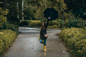 Woman holding a yellow suitcase and an umbrella walking in the park
