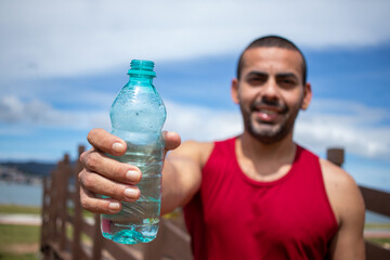 Athletic young man refreshing himself with water after running in blue sky natural landscape background. Healthy lifestyle