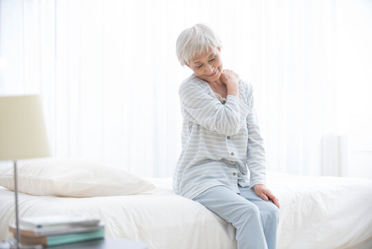起床し肩を揉むパジャマのシニア女性