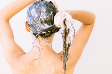 A woman standing in the shower shampooing her hair with water and shampoo.