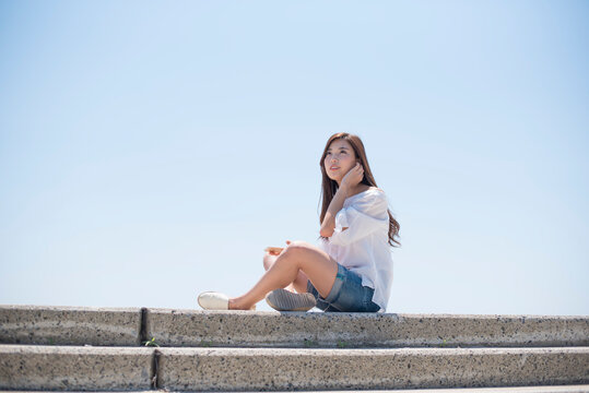 海の堤防に座ってスマホで音楽を聴く女性