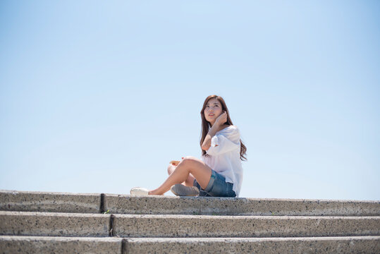 海の堤防に座ってスマホで音楽を聴く女性