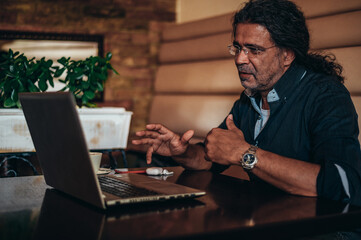 Senior hispanic cuban men using laptop while working remotely in a cafe