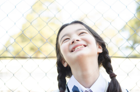 フェンスをバックに上を向いて笑う制服姿の女の子