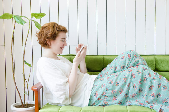 ソファに座ってスマートフォンを操作するハーフの女性