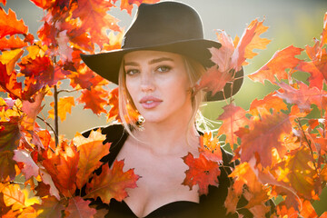 Autumn woman with yellow maple leaves on golden fall background. Close up portrait of a beautiful girl in hat near autumn leaves. Pretty romantic autumn female model.