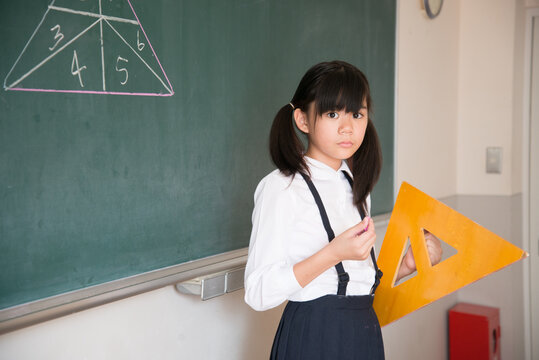 黒板の前で三角定規を持っている小学生の女の子