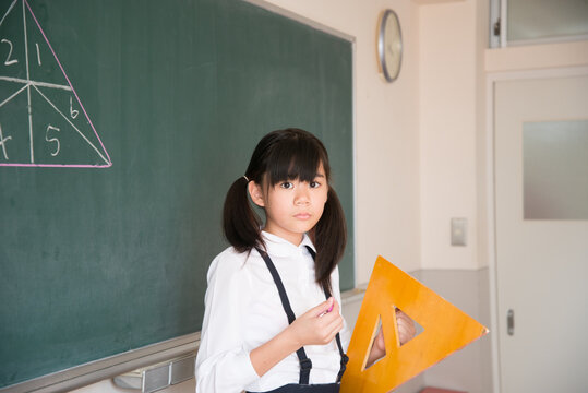 黒板の前で三角定規を持っている小学生の女の子