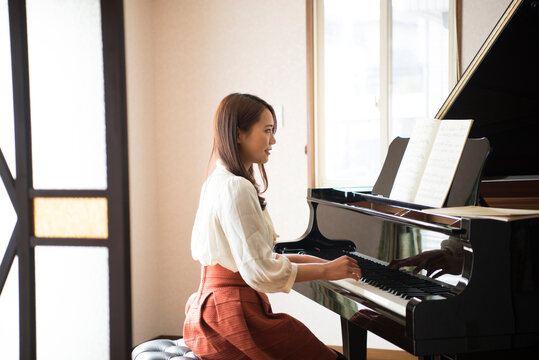 室内でグランドピアノを弾いている女性