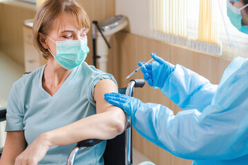 elderly woman patient getting covid-19 or coronavirus vaccine in a wheelchair ​at the hospital.