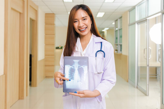 portrait of smart female doctor holding tablet to show X-Ray picture and standing at reception of the hospital.