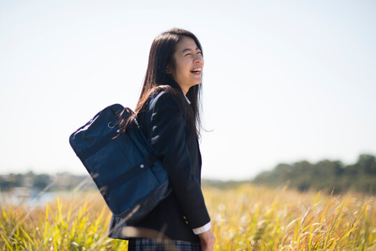 草原に立って笑っている制服姿の女子高生