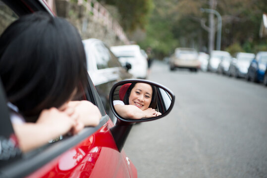 車のサイドミラーを見て笑っている女性