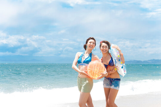 波打ち際でビーチボールと浮き輪を持っている女性2人