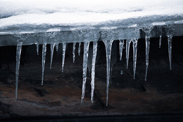 Icicles on roof. Dangerous icing. Ice stalactites on house. Poor maintenance of residential buildings in winter.
