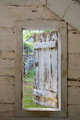 Rural garden viewed through partially open window with weathered wooden shutter and walls