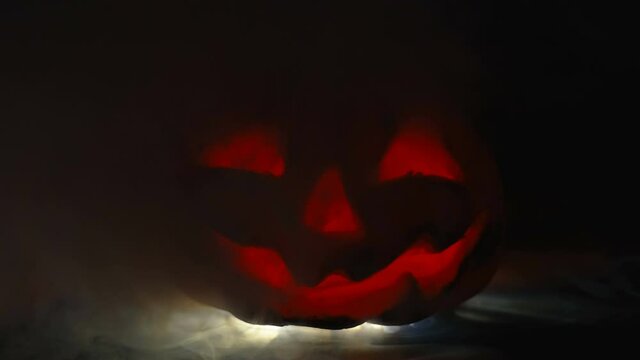 A scary pumpkin face with the red light and smoke inside the dark room on a halloween