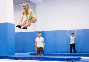 Focused female gymnast jumping on professional trampoline, exercising L shape in jump during training