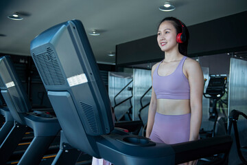 A young woman walks on a treadmill listening to music with headphones to relax happily